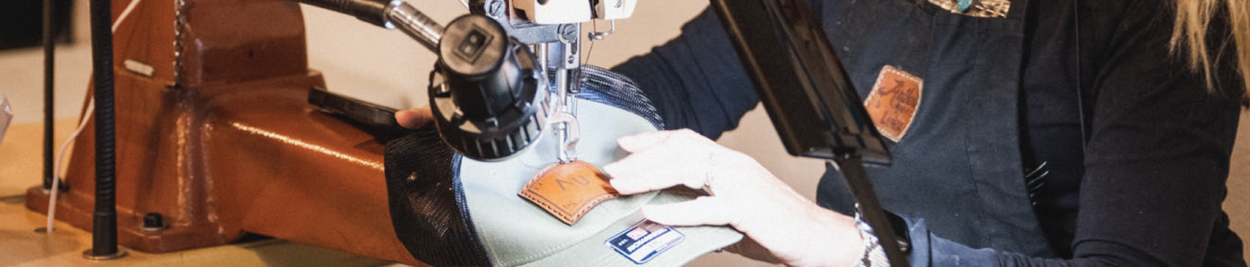 leather patch getting stitched onto a hat with a saddle stitcher by a women